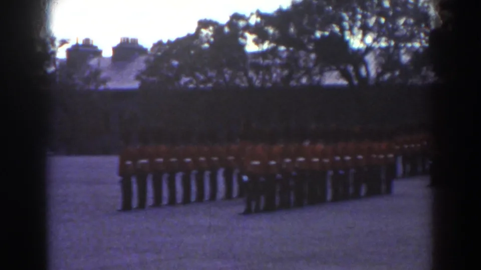 Rows of red-coated guards stand in ceremonial formation in a Quebec courtyard, with trees and rooflines behind them.