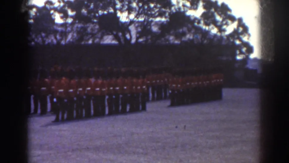 1938 Quebec home-movie frame showing red-coated soldiers in formation on an open field with trees behind them.