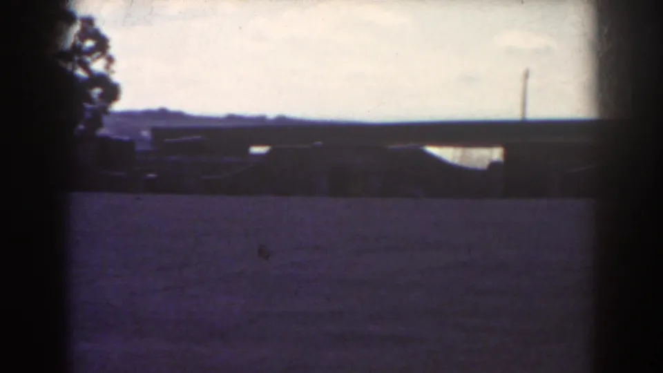 1938 Quebec frame with the formation mostly off to the left and the open field, trees, and distant low structures visible.