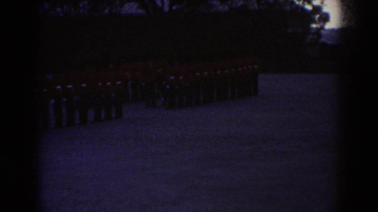 Underexposed 1938 Quebec home-movie frame showing red-coated soldiers lined up near trees on an outdoor field.