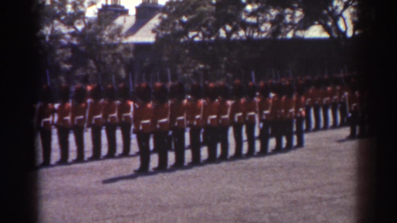1938 Quebec home-movie frame showing uniformed men in red tunics standing in formation with rifles in a courtyard.