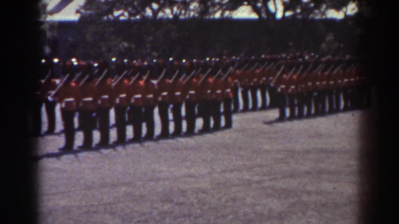 1938 Quebec frame showing uniformed men in red tunics with rifles raised or angled in unison during a ceremonial drill.