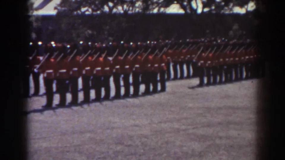 1938 Quebec frame showing uniformed men in red tunics with rifles raised or angled in unison during a ceremonial drill.