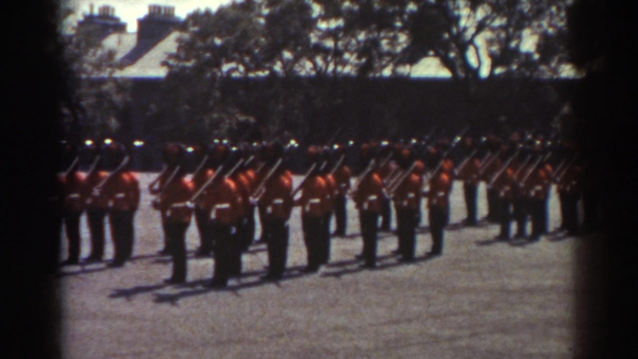 1938 Quebec home-movie frame showing soldiers in red uniforms and dark hats lined up with rifles on a sunlit parade ground.