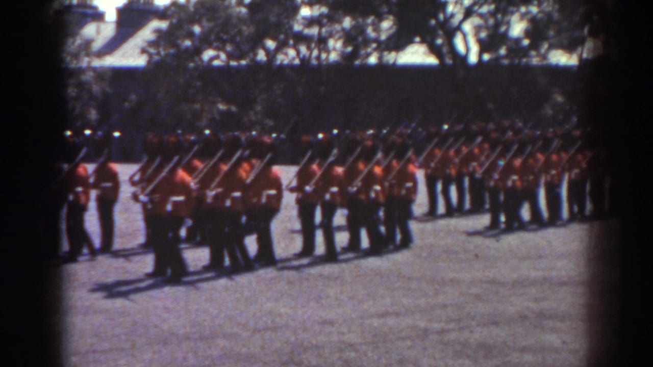 1938 Quebec frame of uniformed soldiers in red tunics arranged in ranks, with rifles and trees visible behind them.