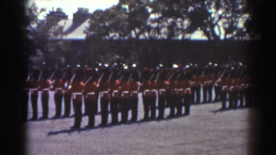Rows of red-uniformed men with black hats and rifles stand in a Quebec ceremonial drill formation.