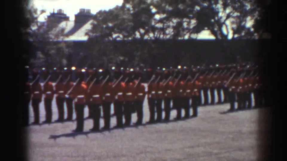 Rows of uniformed guards in red coats and tall dark hats stand with rifles on a sunlit courtyard in the supplied Quebec 1938 footage.