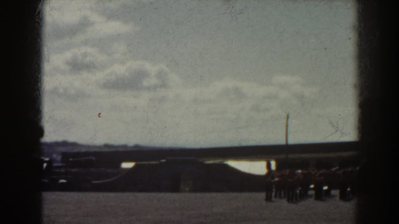 1938 Quebec frame with a small group of uniformed figures at the right edge of a broad sunlit plaza, seen through dark film borders.