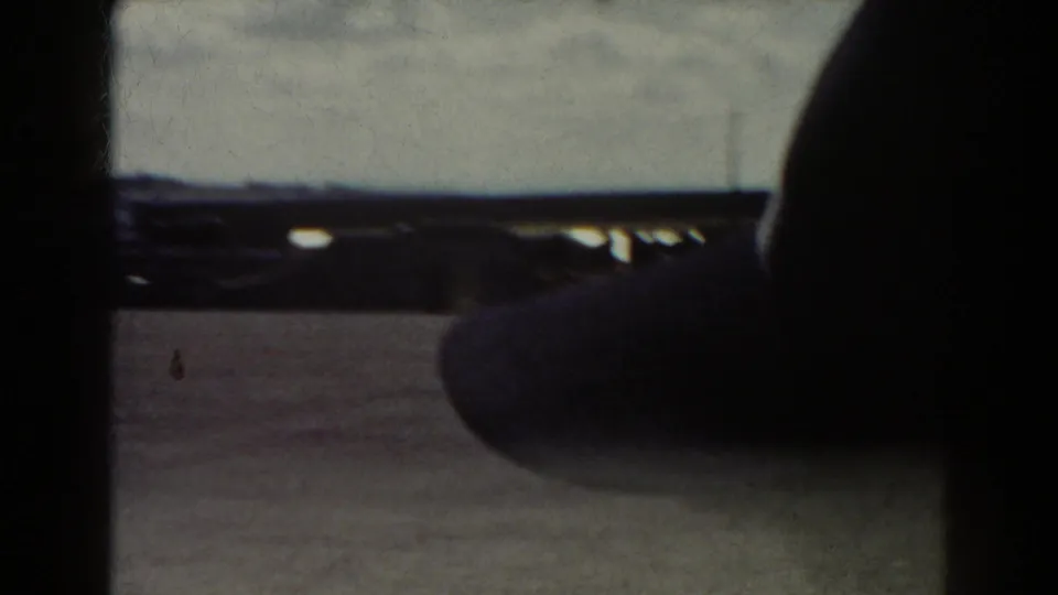 Obstructed 1938 Quebec home-movie frame showing a paved plaza and distant structures, with a dark foreground shape covering much of the scene.