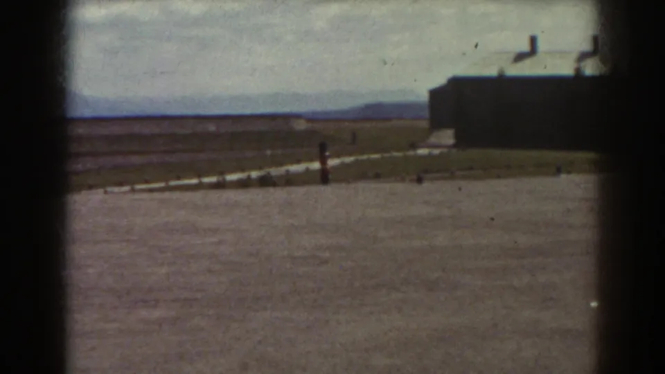 1938 Quebec home-movie frame showing the parade ground after the band has moved out of view, with distant landscape and dark building edge.