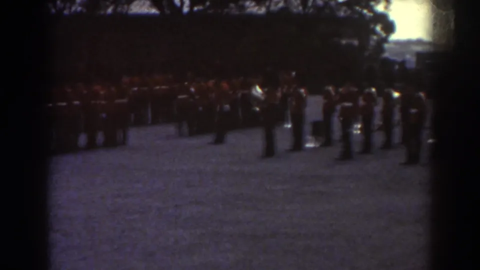Uniformed soldiers in Quebec stand in long formation on a gravel field, with several figures gathered to the side.