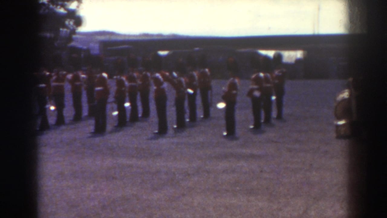 Uniformed band members remain lined up outdoors with instruments visible.