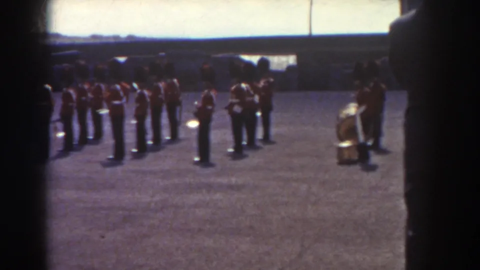 A 1938 Quebec band formation continues on a gravel field, with drums and brass players partly framed by a dark foreground edge.
