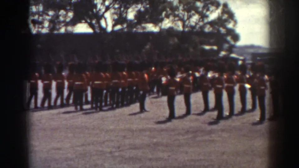 Quebec 1938 home-movie frame of ceremonial soldiers in red tunics standing in ordered lines under strong daylight.