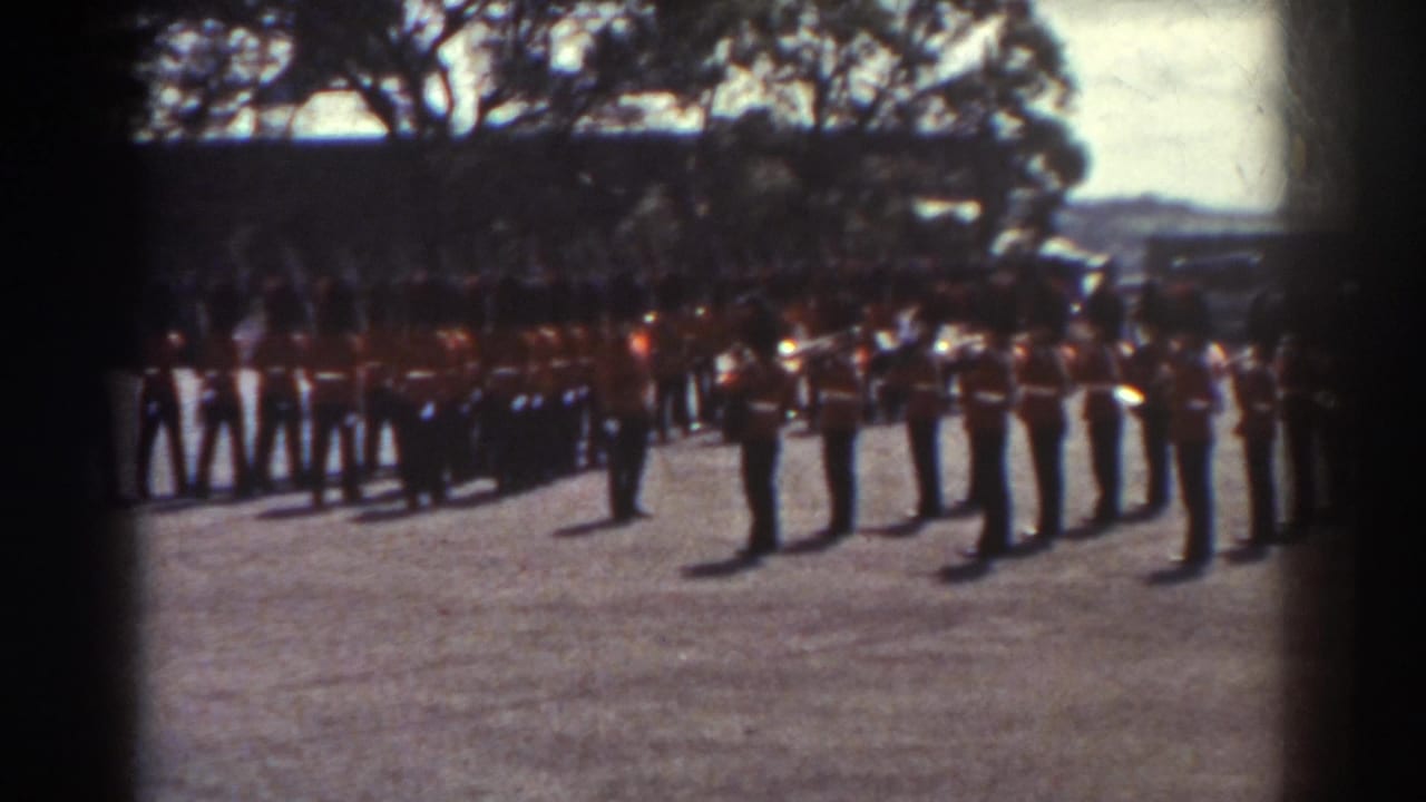 1938 Quebec home-movie frame showing ceremonial guards in red tunics and tall dark hats lined up outdoors.