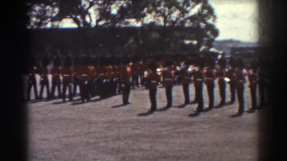 1938 Quebec home-movie frame showing ceremonial guards in red tunics and tall dark hats lined up outdoors.