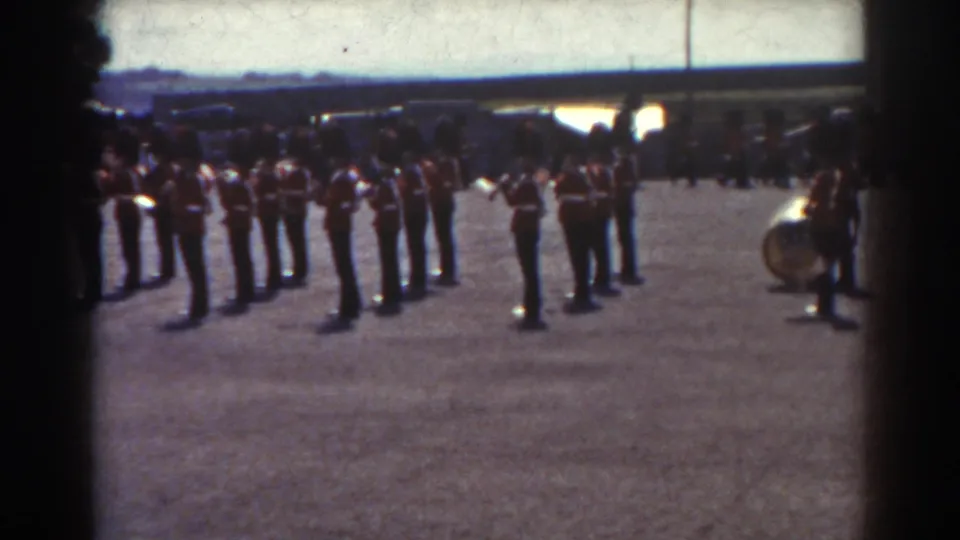 Quebec 1938 home-movie frame showing guards in red tunics lined up with musicians and a large brass instrument nearby.