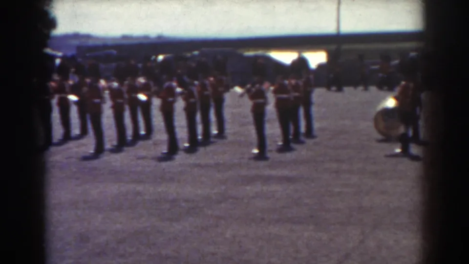 1938 Quebec home-movie frame showing uniformed soldiers in ranks on a gravel field, seen through dark foreground edges.