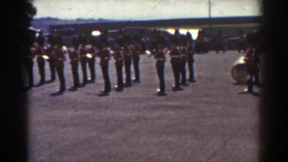 1938 Quebec footage frame with soldiers or band members standing in formation, softly focused and bordered by dark foreground edges.