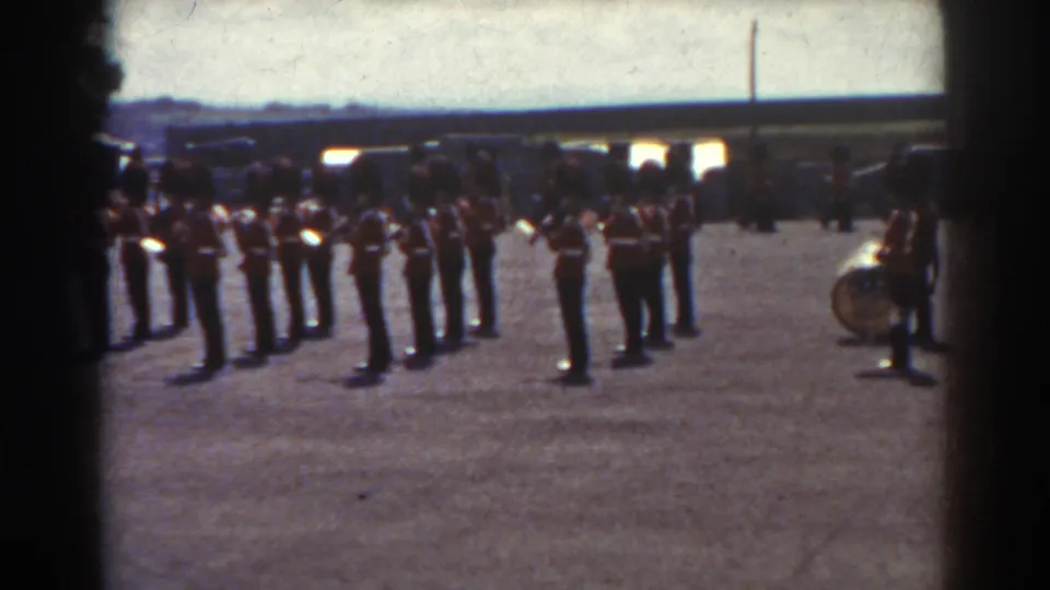 Late-1930s Quebec home-movie frame showing uniformed soldiers in formation, with a large drum near the right edge.