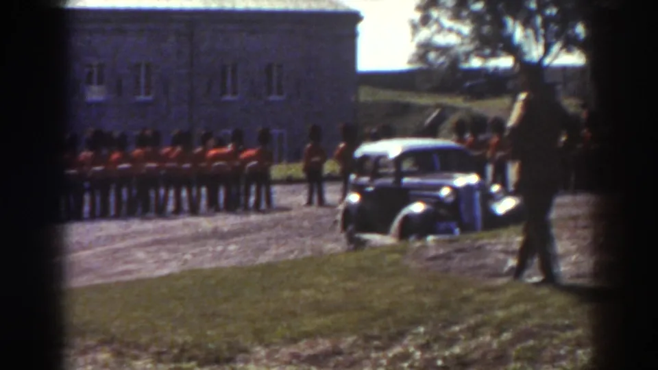 1938 Quebec home-movie view of red-coated soldiers, a period automobile, and a walking figure in the courtyard.