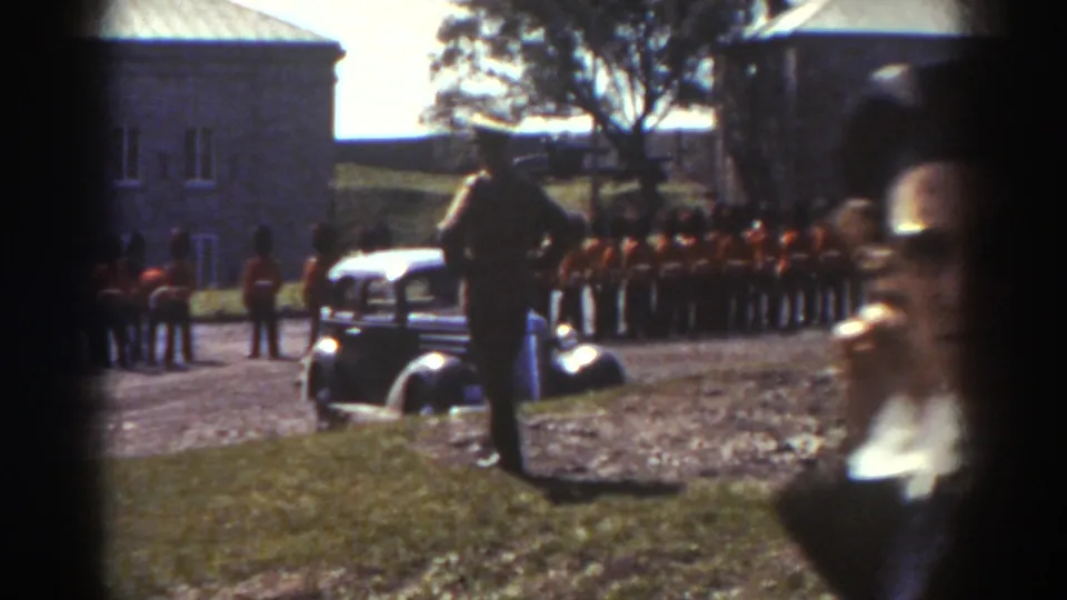 1938 Quebec frame showing soldiers in formation behind a period car, with bystanders partly visible in the foreground.