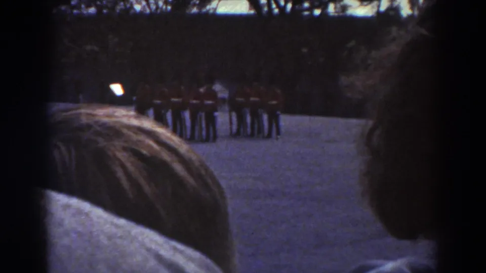 Soft 8mm Quebec 1938 view of guards in dark uniforms and tall hats, seen over spectators gathered near the camera.