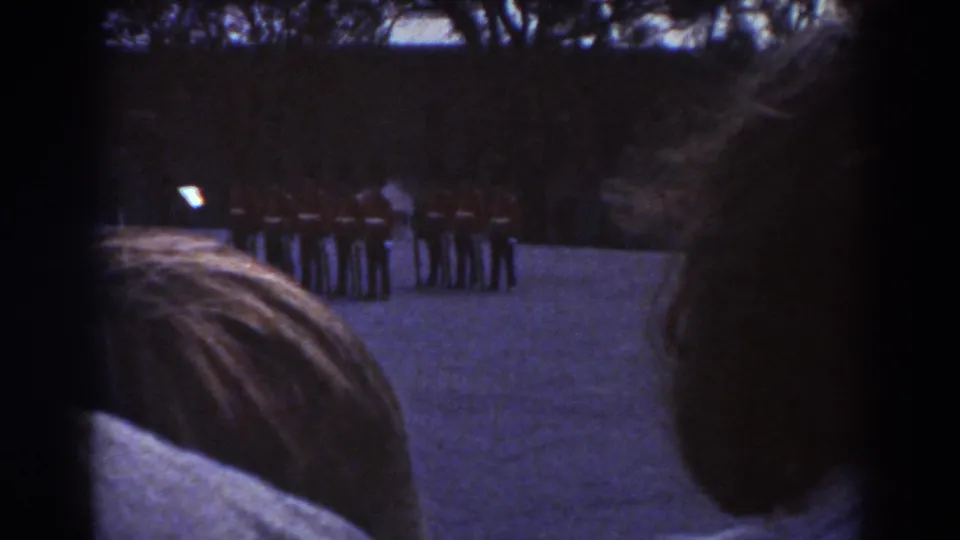 Quebec 1938 home-movie frame with a dark spectator silhouette at right and ceremonial guards lined in a semicircle beyond.