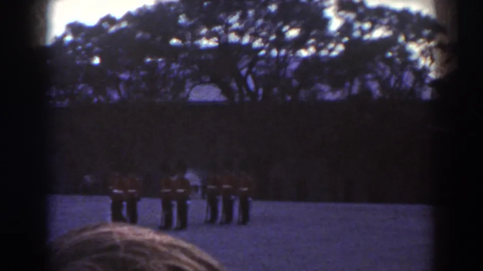 The final still keeps the Quebec drill at a distance, with red-coated soldiers framed by foreground spectators and dark film-edge shadows.