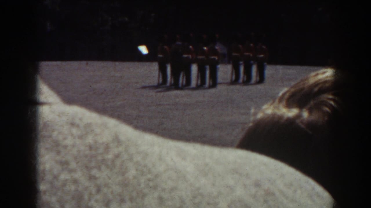 In 1938 Quebec home-movie footage, foreground spectators partially block a distant group of uniformed soldiers on a sunlit field.