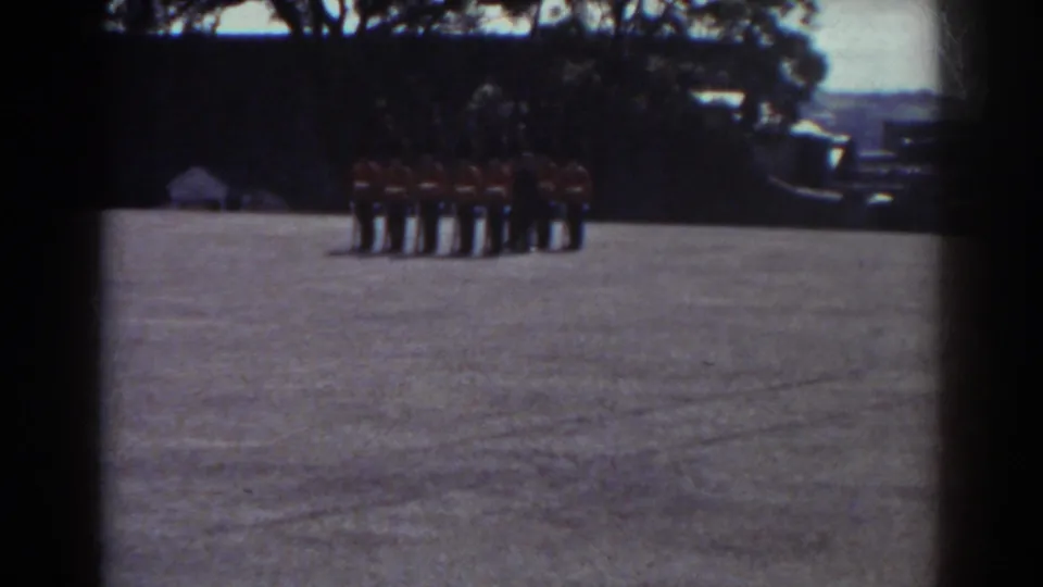 The camera settles on a line of uniformed soldiers in red coats and dark trousers standing on an open Quebec field.
