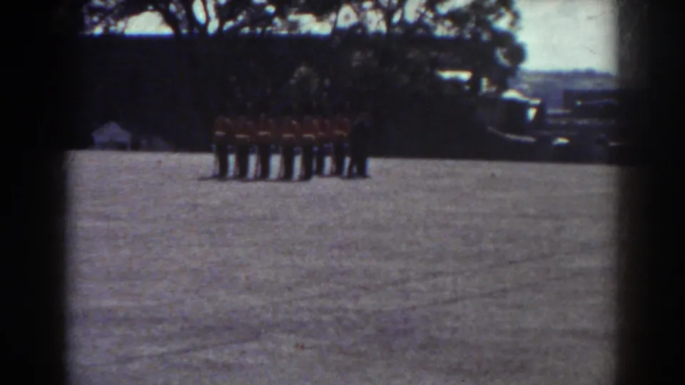 Uniformed soldiers remain grouped in formation on a broad field, with trees and distant landscape visible behind them.