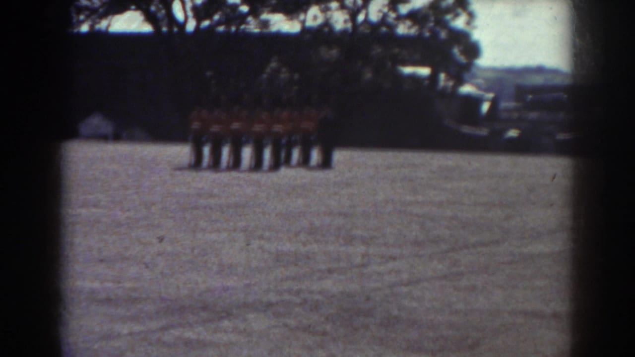 In Quebec, Canada, uniformed guards in red tunics and tall black hats stand at attention on a broad gravel courtyard.