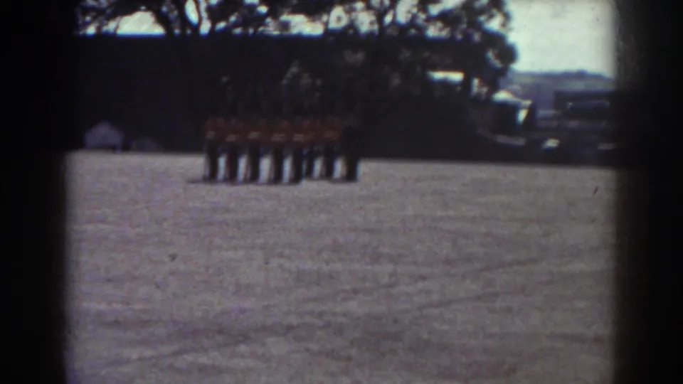 In Quebec, Canada, uniformed guards in red tunics and tall black hats stand at attention on a broad gravel courtyard.