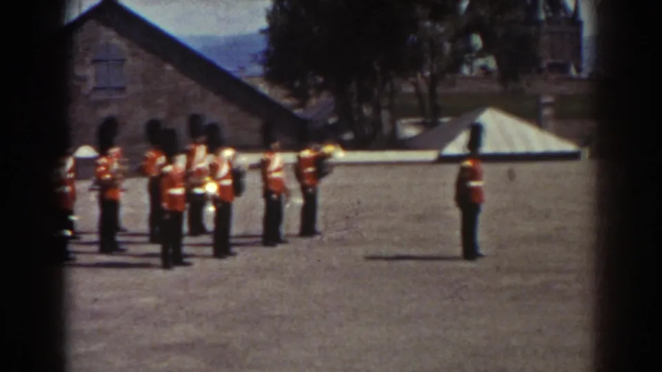 A closer view shows uniformed guards in red tunics and tall hats grouped in formation on the Quebec gravel courtyard.