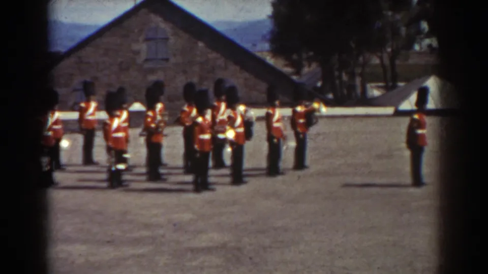 Uniformed guards stand together in a Quebec courtyard, with one guard positioned separately to the right near the open gravel space.