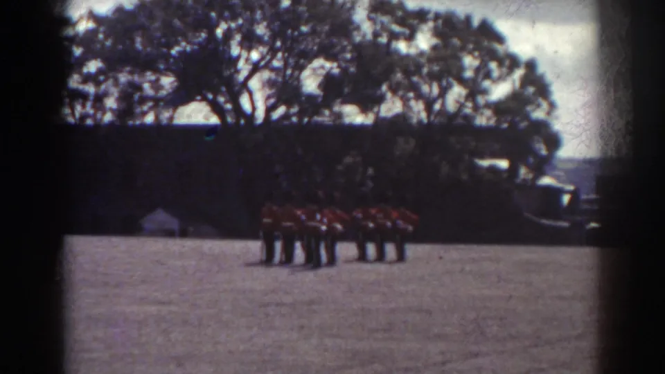 The final frame shows a darker, more distant view of red-uniformed figures grouped near trees at the edge of the courtyard in the same Quebec home-movie clip.