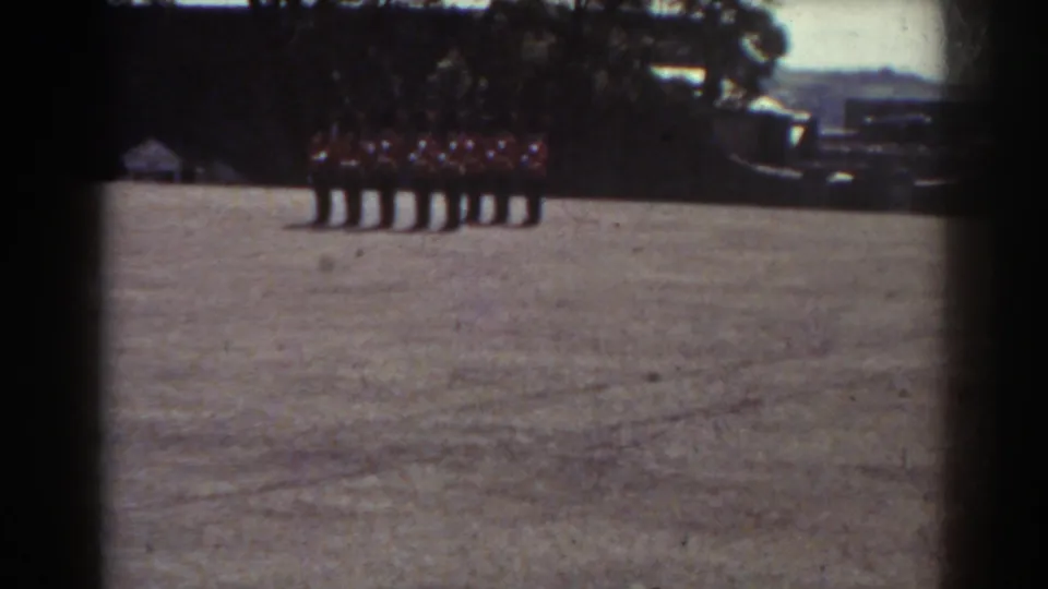 1938 Quebec 8mm frame showing a row of uniformed people standing together on a field with trees behind them.
