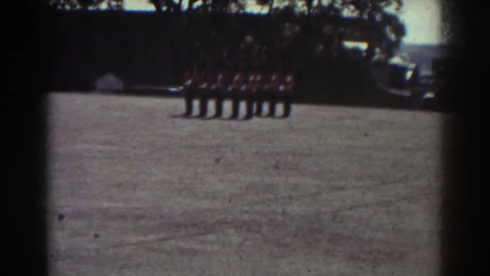 1938 Quebec home-movie frame with a distant uniformed line standing on a field under bright daylight.