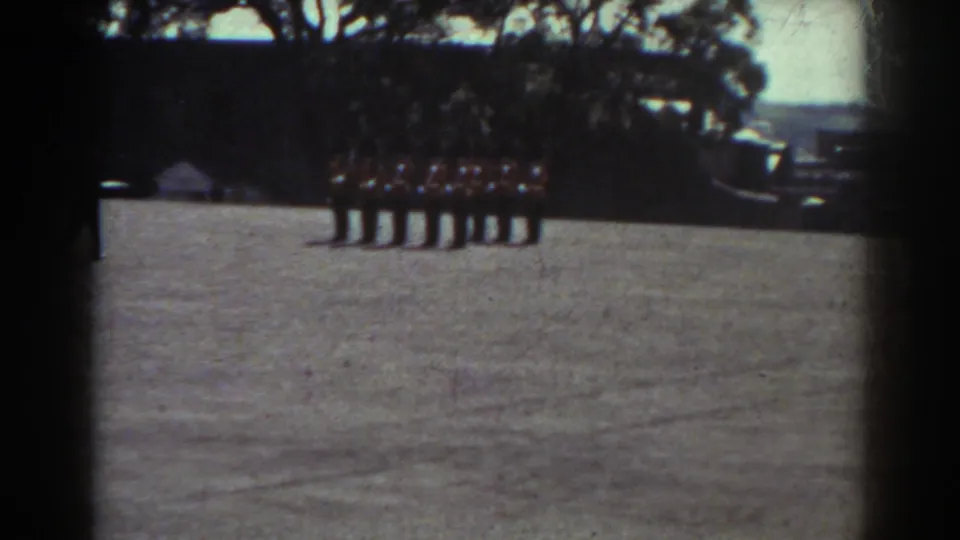 In Quebec 1938 home-movie footage, uniformed men stand at attention on a field with trees and possible vehicles in the background.