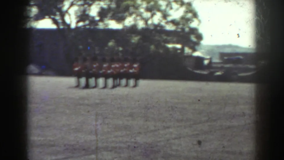 Quebec 1938 8mm frame showing a line of uniformed men on a field, with a small tent-like shape to the left and trees behind.