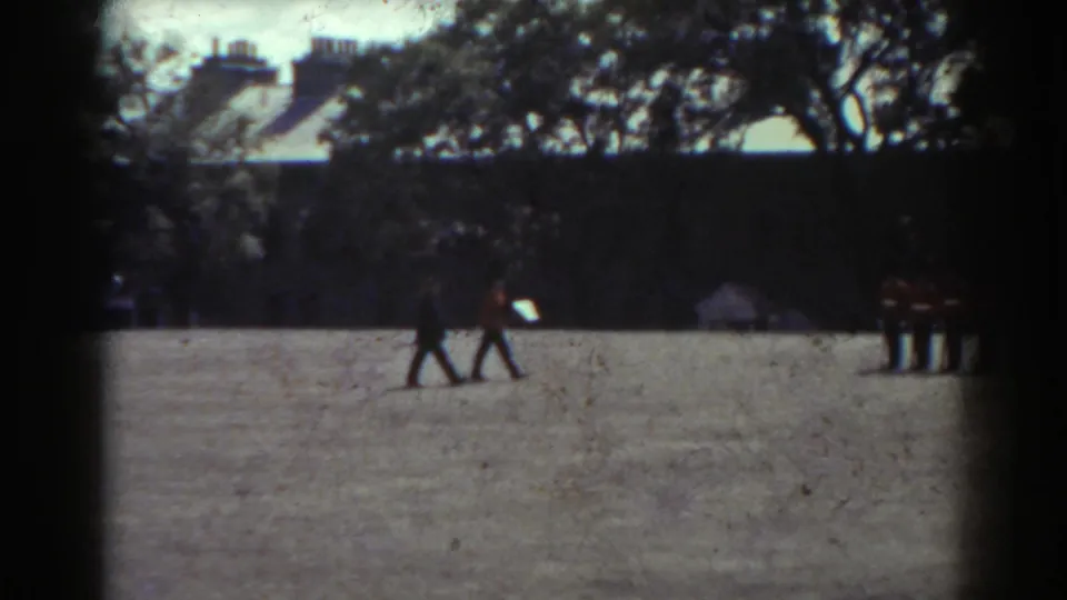 1938 Quebec home-movie view of two figures crossing a gravel courtyard while guards remain partly visible near the frame edge.
