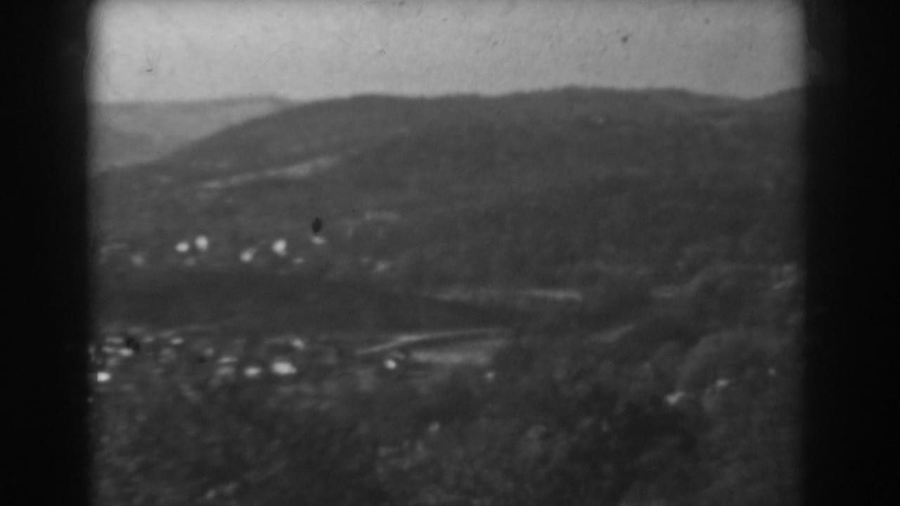 Distant hillside landscape with scattered houses, tree cover, and dark film edges.