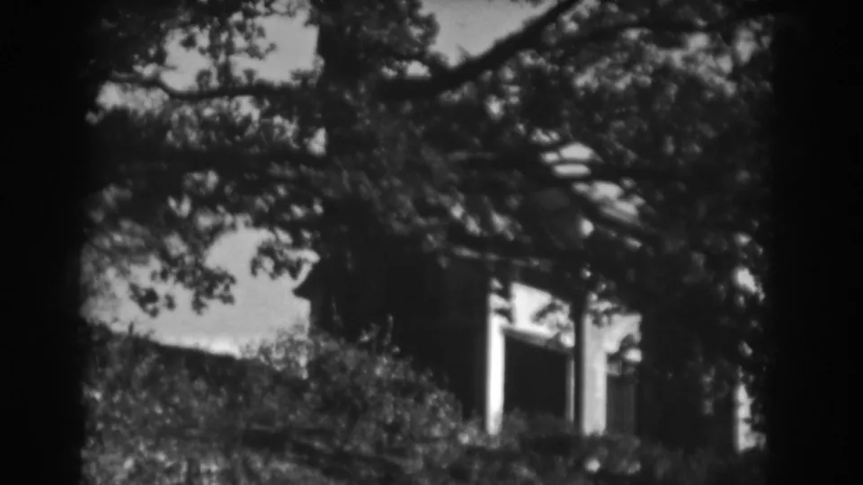 Black-and-white 1938 Vineland home-movie frame with a white building partly obscured by trees.