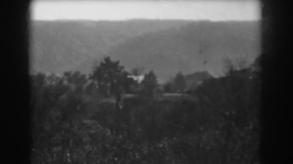 1938 Vineland home-movie still showing brush in the foreground, scattered trees, distant hills, and soft exposure within dark 8mm borders.
