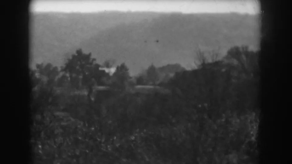 Final 1938 Vineland, New Jersey frame holds on a soft rural view of trees, low hills, brush, and faint distant structures.