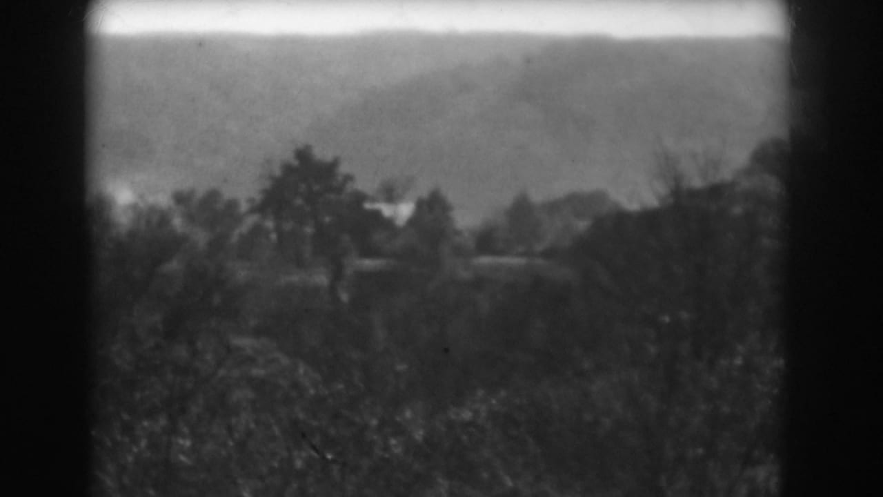 Black-and-white 8mm frame showing a hazy rural valley near Vineland with distant trees and dark gate edges.