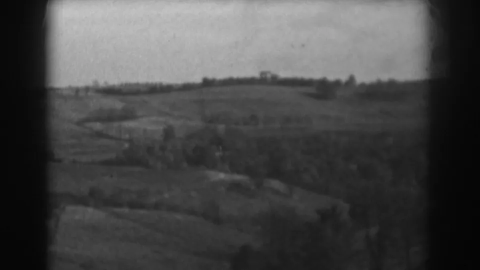 1938 black-and-white 8mm view near Vineland showing open fields, a distant treeline, and a small structure on the horizon.