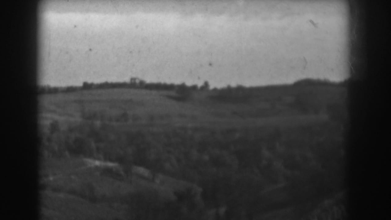 Wide countryside view with fields, trees, low ridge, and dark rounded film borders.