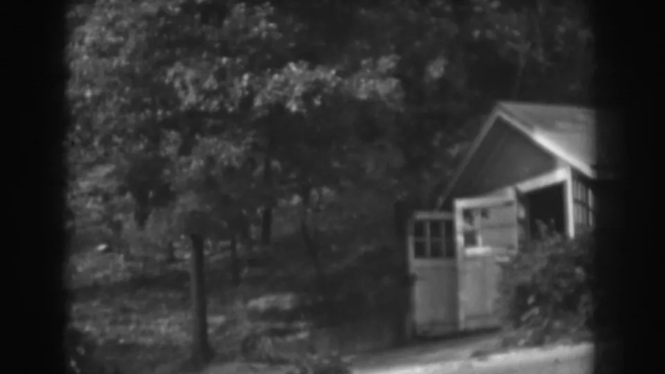 1938 Vineland, New Jersey frame showing a small shed, leafy trees, bright yard edge, and a person partly visible near the doorway.